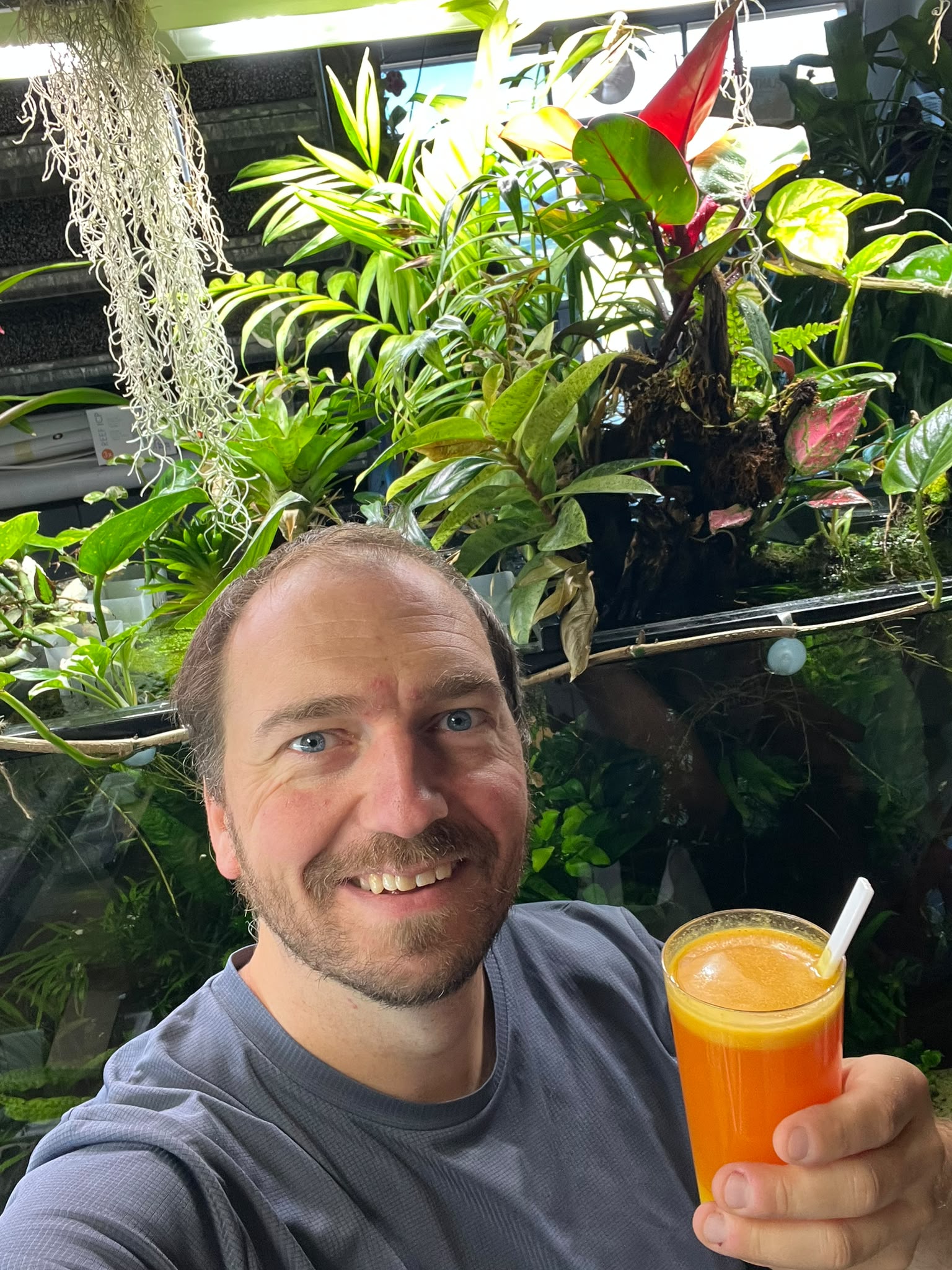 Jérôme, souriant devant les plantes, un verre à la main